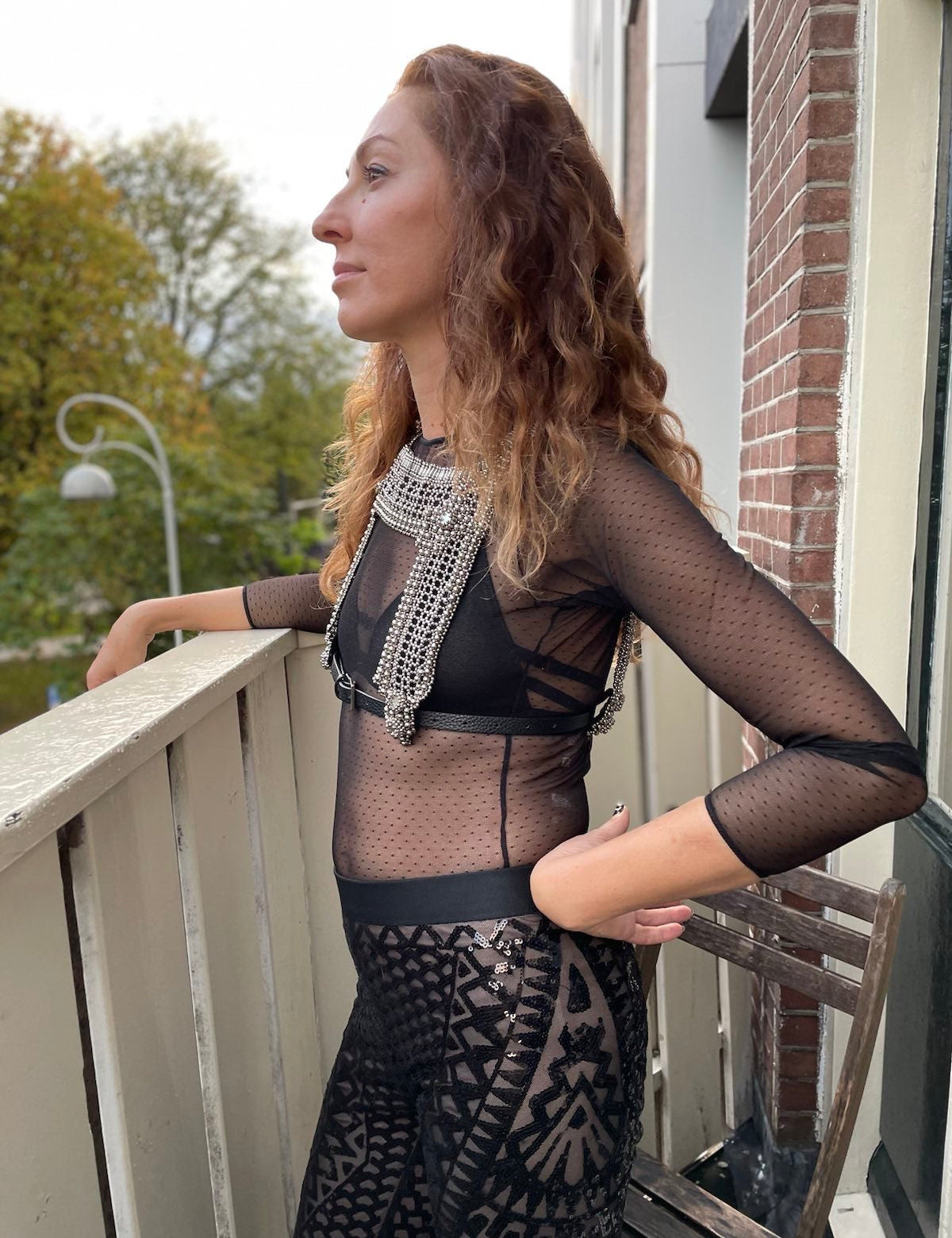 Saida Mouradova standing on a balcony wearing the Artemisia Mesh Top in Silver.