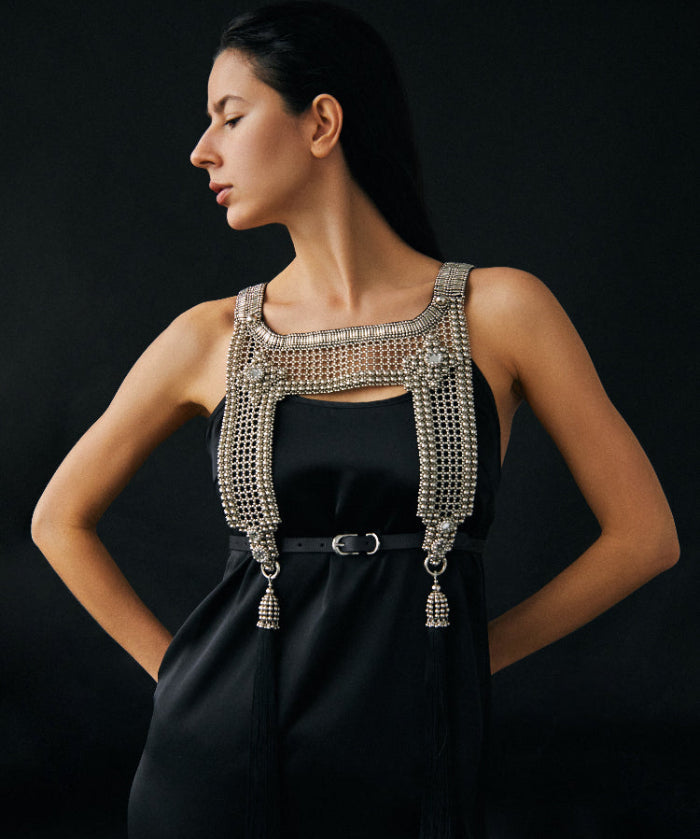 Woman wearing a black dress with a beaded silver harness against a dark background