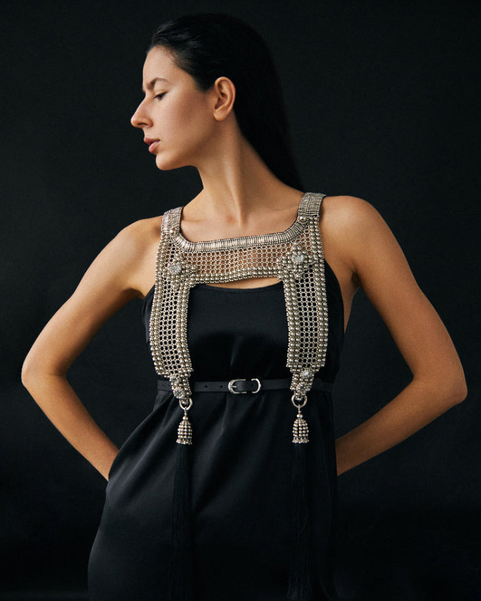 Woman wearing a black dress with a beaded silver harness against a dark background