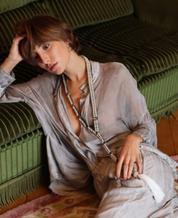 Woman in a light-colored outfit sitting on a green couch with a pearl beaded necklace.