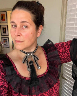 Woman wearing a red and black patterned top with a beaded Amaya Bow Choker. 
