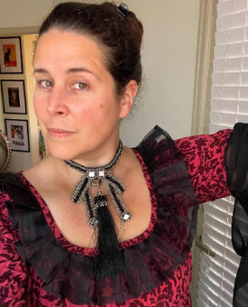 Woman wearing a red and black patterned top with a beaded Amaya Bow Choker. 