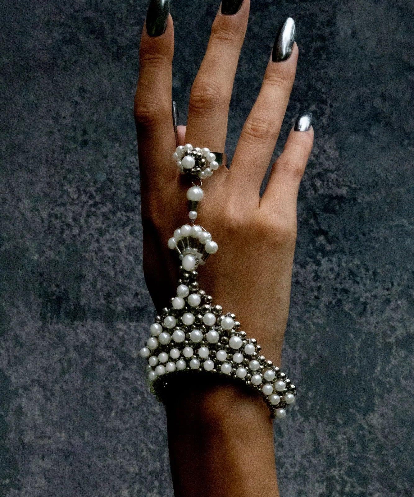 Hand wearing a decorative pearl bracelet and ring against a dark textured background