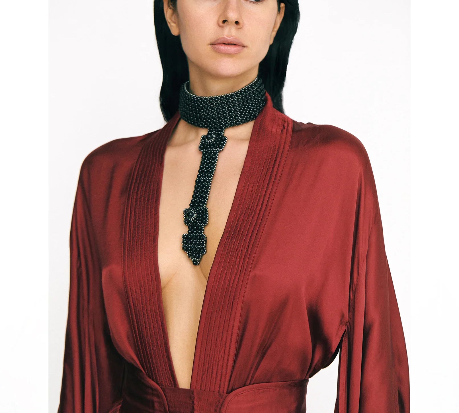 Woman wearing a burgundy short silk kimono and a black beaded necklace on a white background