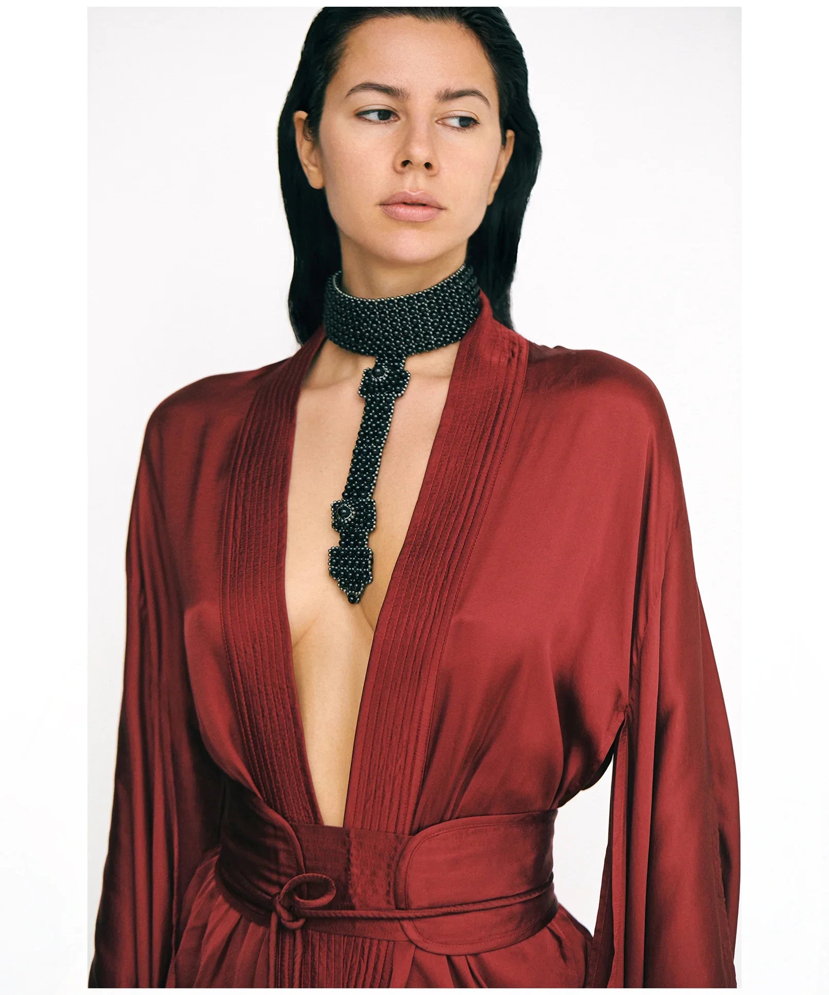 Woman wearing a burgundy short silk kimono and a black beaded necklace on a white background