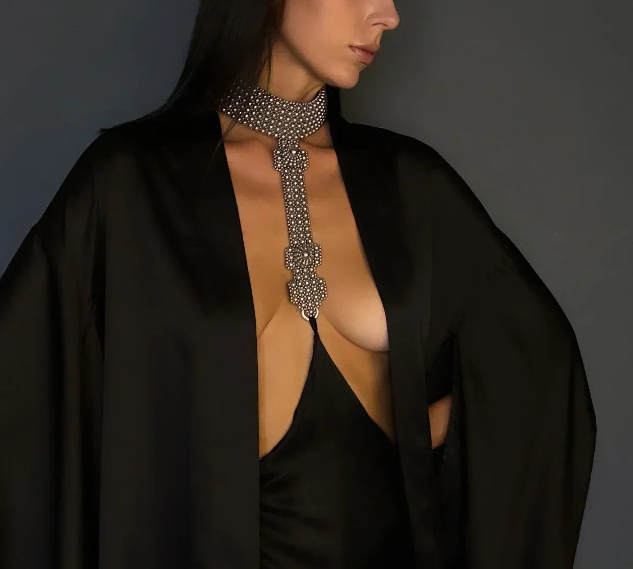 Woman wearing a black silk skirt connected to a silver beaded necklace against a gray background