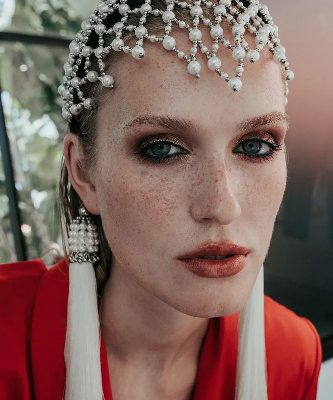close up woman wearing a red outfit with decorative freja headbandand earrings against a plain background