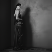 Woman in a long dark dress standing against a textured wall with a dramatic shadow.