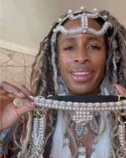 Black woman wearing beaded headband and holding a beaded headpieces looking into camera.