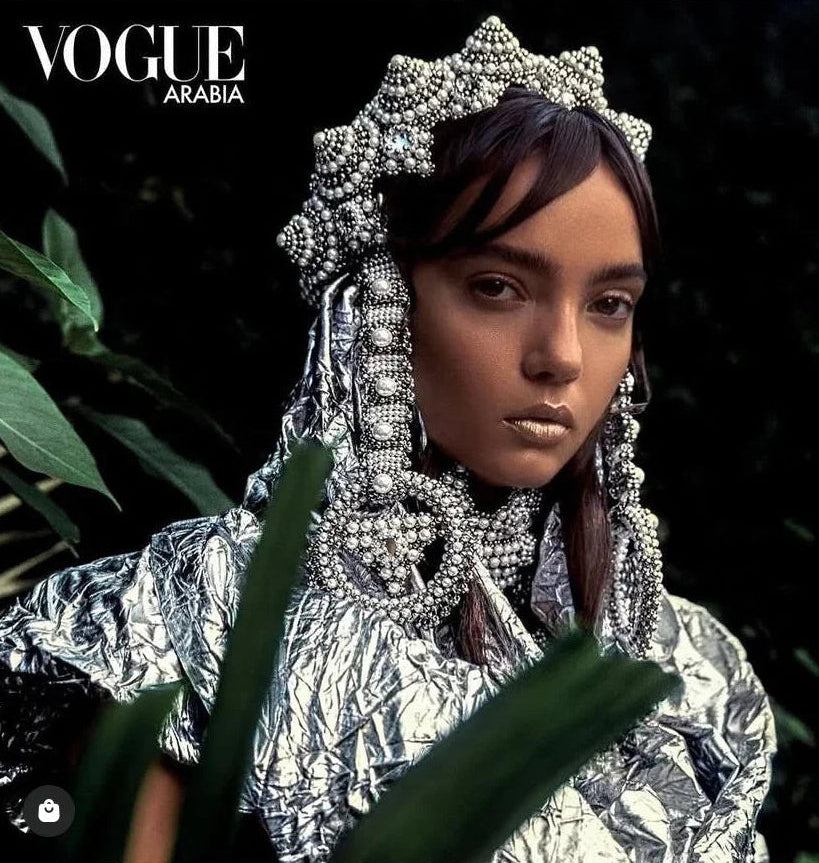 Person wearing a silver headpiece and foil garment with 'Vogue Arabia' logo.