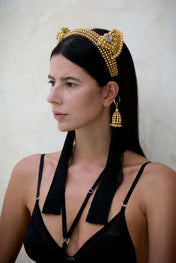 Woman wears Jas Headband gold with 11" tassels gold-black by Object & Dawn in neutral backgorund