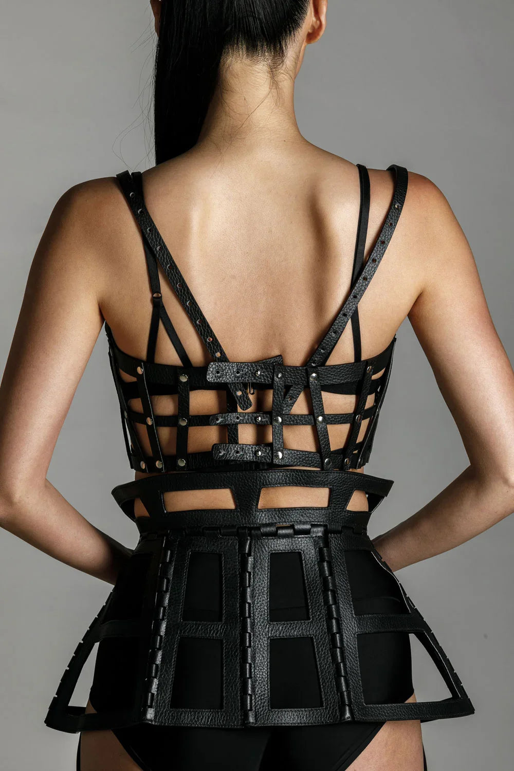 woman with premium leather studded cage top black on grey background back view close up
