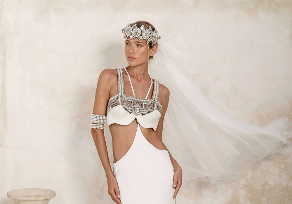 Woman wearing a white and silver bridal outfit with a headpiece and silk skirt by Object &amp; Dawn. background is netral