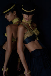 Two women in elaborate costumes with Elohim T-Choker, Khutulun Modular Top with Leather Bra, Artemisia 4D Supple Cuff, and Hatbanc Gold by Object & Dawn against a dark background