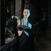 A woman wearing Object & Dawn beaded accessories in black with black silks clothing in a dark, industrial setting