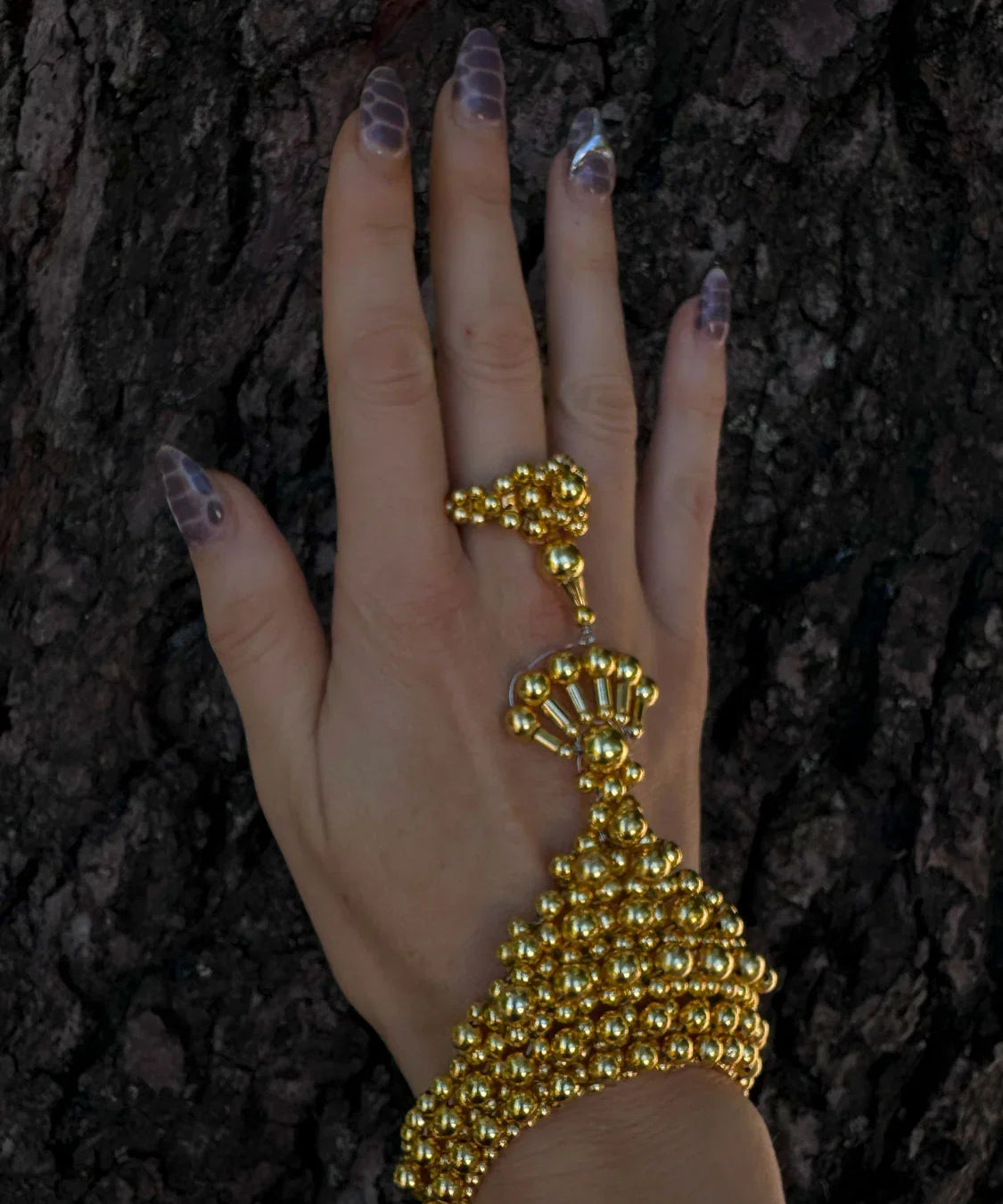 luxury beaded hand jewelry with 22k gold wash on polymer metal beads on hand with wood background by object and dawn