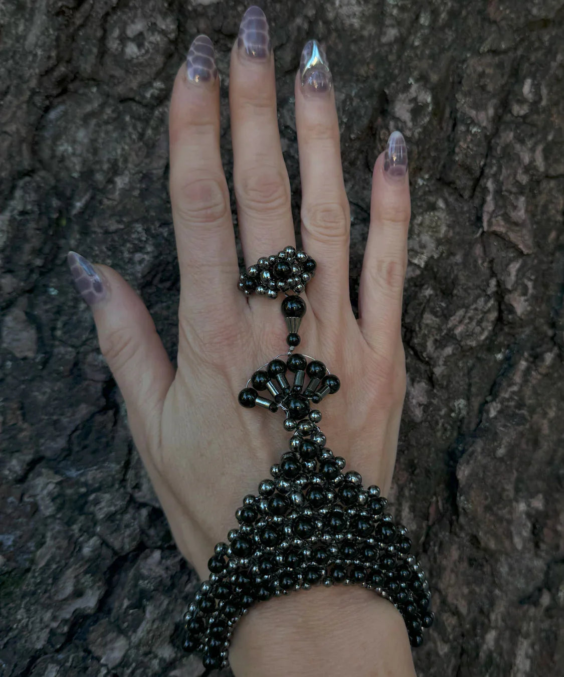 handcrafted beaded hand jewelry polymer metal beads and crystal black on hand with wood background by object and dawn