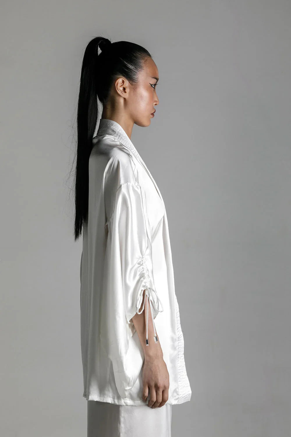 short white silk kimono worn on woman by object and dawn at neutral background side view