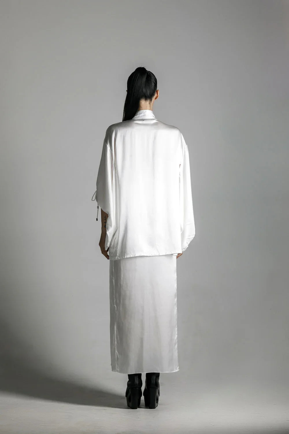 short white silk kimono with white harness skirt worn on woman by object and dawn at neutral background back view