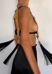 Torso of woman spinning while wearing gold beaded harness. Gold capped black threaded tassels float with spinnning motion. white background