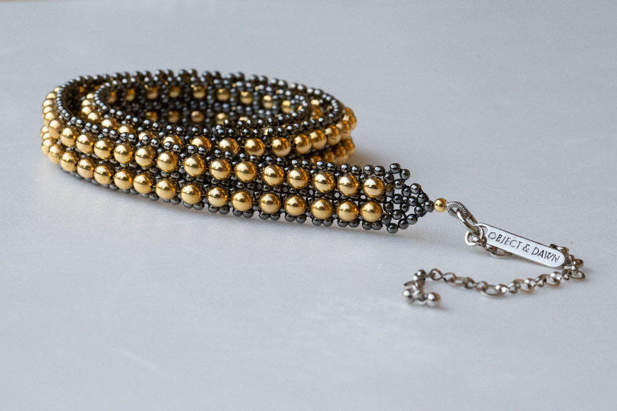 Beaded gold and gunmetal hatband coiled and resting on a white table. 