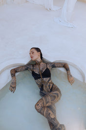 woman with tattoes wear t shape choker harness antique gold by object and dawn in pool background