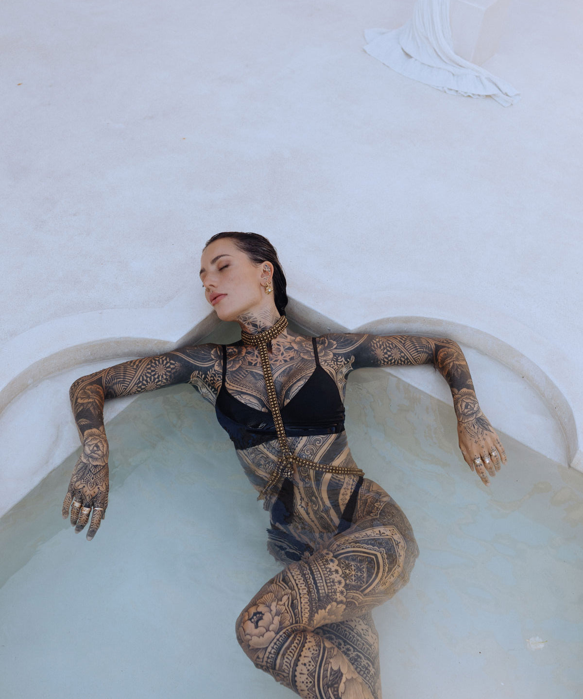 woman with tattoes wear t shape choker harness antique gold by object and dawn in pool background
