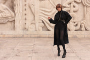 Woman wearing a black outfit and V-Shape Beaded Harnessstanding in front of stone sculptures by Object & Dawn